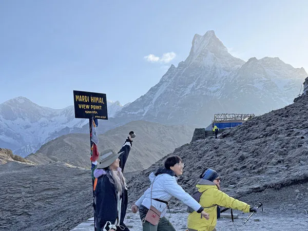 Happy trekkers posing near the Mardi Himal View Point 4200m sign board with Mount Machhapuchhre Fishtail in the background.
