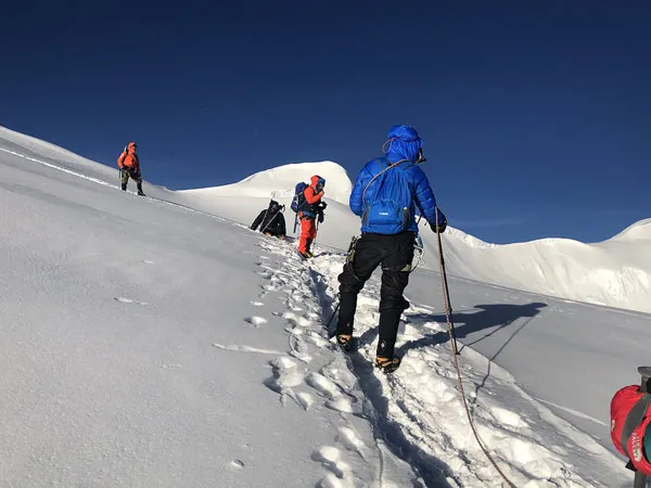 A roped group of high-altitude climbers in warm winter gear ascending a steep snowfield on Mera Peak