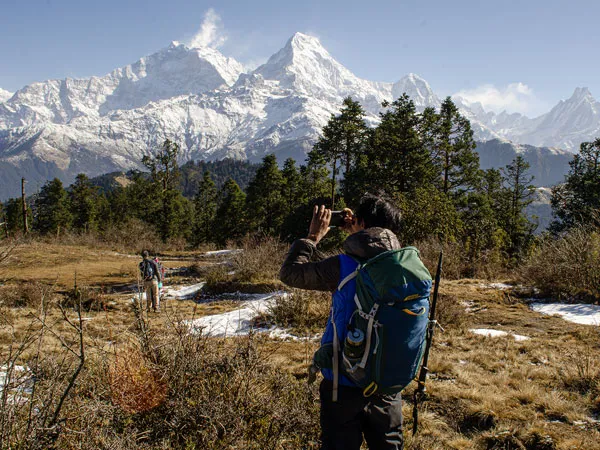 A trekker with a backpack taking a photo of snow-capped Annapurna mountains during the Mohare Danda Trek