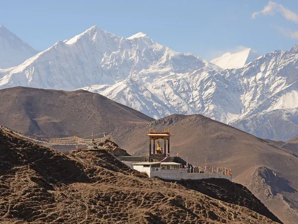 Scenic view of Muktinath shrine and colorful prayer flags with snow-capped Himalayan mountains in the background during the Jomsom Muktinath Trek