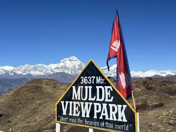 Mulde View Park sign (3,637 m) featuring the flag of Nepal with snow-covered mountain peaks under a clear sky.