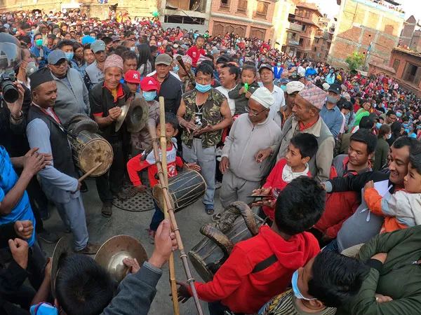 A large crowd gathered in a traditional Newar square celebrating with traditional percussion instruments and brass cymbals