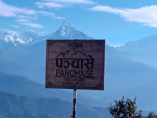 Wooden Panchase welcome sign showing an elevation of 2,517 meters, with the snow-capped peak of Mount Machhapuchhre in the Annapurna range set against a blue sky.