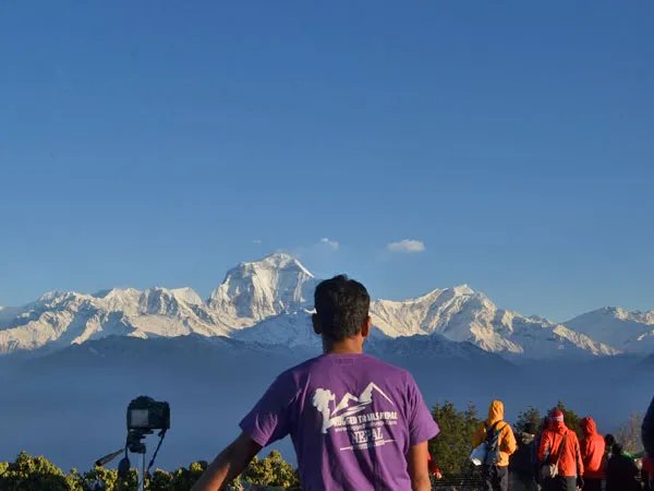 Trekkers and a guide wearing a purple Rugged Trails Nepal t-shirt looking out at the snow-capped Annapurna Himalayan range from Poon Hill during the Short Ghorepani Ghandruk Trek.