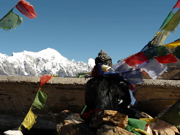 Black Buddha statue adorned with colorful Tibetan prayer flags framed against snow-capped Himalayan peaks on the Short Gosaikunda Lake Trek in Nepal
