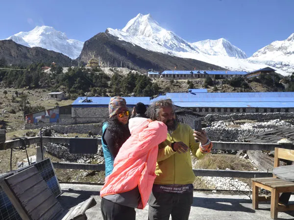 Trekkers taking a photo on a mountain lodge terrace in the Himalayas, with blue-roofed village