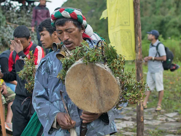 A local Tamang shaman (Dhami/Jhakri) performing a traditional cultural ritual with a leaf-adorned drum and headpiece during the Tamang Heritage Trek in Nepal.