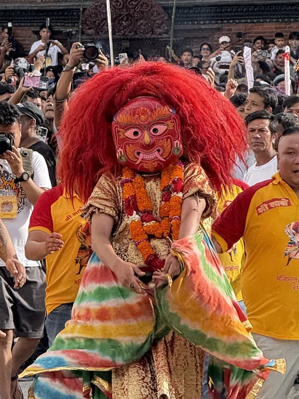 A performer dressed as Majipa Lakhey wearing a fierce red mask with orange hair and marigold garlands performing amidst crowds at the Indra Jatra festival in Kathmandu Durbar Square